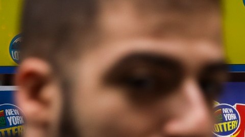 Una persona borrosa camina frente a dos letreros luminosos de las loterías Mega Millions y Powerball, en los que se ve la cantidad de los premios jackpot.