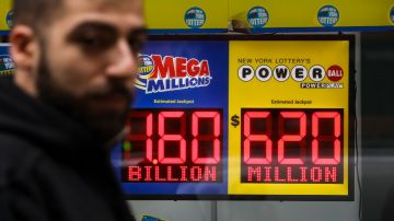 Una persona borrosa camina frente a dos letreros luminosos de las loterías Mega Millions y Powerball, en los que se ve la cantidad de los premios jackpot.