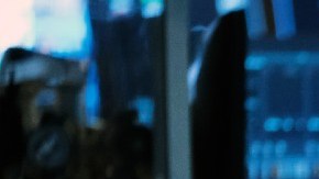 Una persona en el piso de ofertas en Wall Street se lleva la mano al rostro mientras mira pantallas con indicadores.