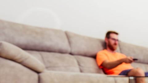 un robot roomba en el suelo de una habitación en la que también hay una persona sentada en un sillón.