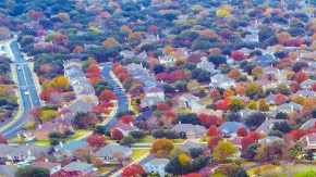 Un grupo de viviendas se ven desde el aire, en medio de un lugar arbolado y con jardines.