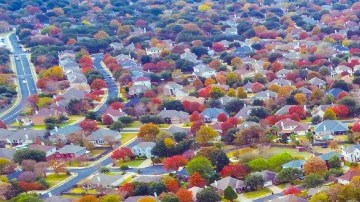 Un grupo de viviendas se ven desde el aire, en medio de un lugar arbolado y con jardines.