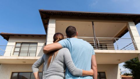 Dos personas se abrazan frente a una casa.