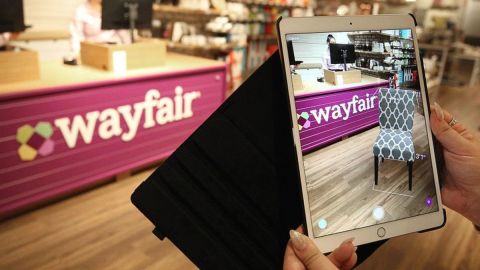 Imagen de una persona que sostiene una tablet que la apunta a un logotipo de la marca Wayfare en color púrpura.