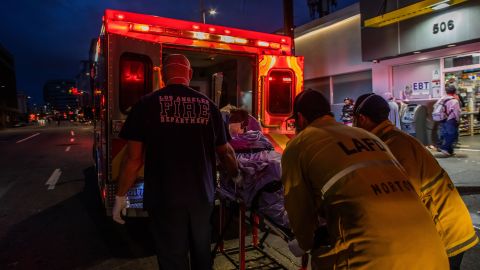 TOPSHOT - Paramedics of the LAFD Station No9 wear a face mask as a preventive measure against the spread of the COVID-19 novel coronavirus from a homeless woman who had seizures on the street at Skid Row, before boarding her in the ambulance to go to a hospital on April 12, 2020 in downtown Los Angeles, California. - One of the busiest fire station in the country , LA Fire Station 9 is on the front lines of California's homeless crisis e Coronavirus pandemic. (Photo by Apu GOMES / AFP) (Photo by APU GOMES/AFP via Getty Images)