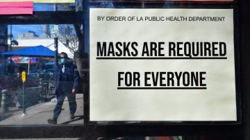 A man wearing a protective face mask walks past a sign requiring face masks posted on a storefront in Los Angeles, California, on March 2, 2022. - Los Angeles County will drop its mask-wearing mandate on March 4, 2022, as mask-mandates relax in California and across the United States. (Photo by Frederic J. BROWN / AFP) (Photo by FREDERIC J. BROWN/AFP via Getty Images)