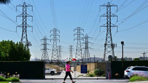 TOPSHOT - A pedestrian uses an umbrella to shield themself from the hot sun while walking past power lines in Rosemead, California, on August 31, 2022. - Temperatures as high as 112 degrees Fahrenheit (44 Celsius) were expected in some Los Angeles suburbs as a huge heat dome bakes a swathe of the western United States. The sweltering weather is expected to put huge demands on the already-stretched power grid, especially when people crank up the air conditioners during the broiling hours after work and school. (Photo by Frederic J. BROWN / AFP) (Photo by FREDERIC J. BROWN/AFP via Getty Images)