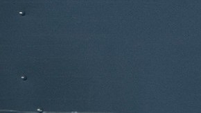 Un hombre vestido con un uniforme de Amazon color azul camina frente a un muro en el que se ve una sonrisa azul y letras blancas con la frase Prime.