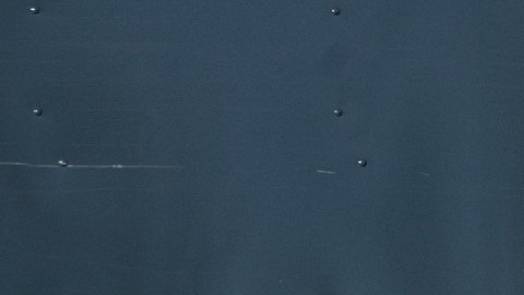 Un hombre vestido con un uniforme de Amazon color azul camina frente a un muro en el que se ve una sonrisa azul y letras blancas con la frase Prime.