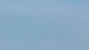 Un barco carguero se acerca aun puerto y en el fondo se ven edificios.