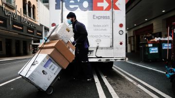 Imagen de un trabajador de FedEx mientras empuja unos paquetes, frente a un camión de la compañía.