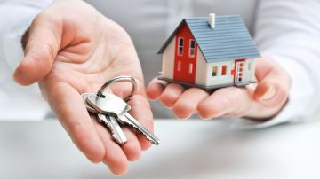 Una persona muestra con su mano unas llaves y con la otra sostiene una casa en miniatura.