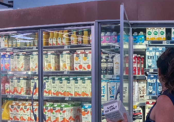 Una persona abre un refrigerador en un supermercado y sostiene con la mano un envase.