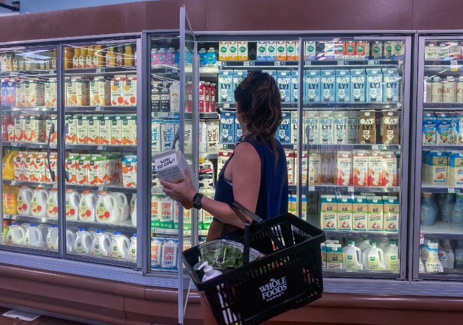 Una persona abre un refrigerador en un supermercado y sostiene con la mano un envase.