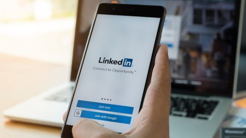 Imagen de un teléfono celular con un logotipo de LinkedIn, delante de una computadora personal.