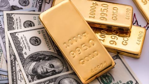 Imagen de tres lingotes de oro sobre varios billetes.