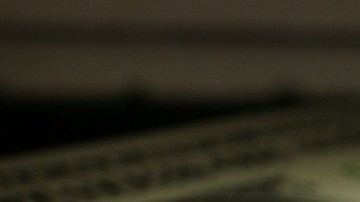 Imagen de dos casas de plástico de color verde junto a otra de color rojo, sobre billetes de dólares.