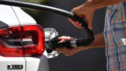 Imagen de una persona que sostiene una pistola despachadora de gasolina mientras surte combustible en un vehículo blanco.