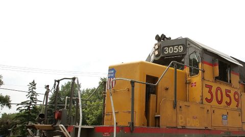 Un tren de color amarillo cruza un paso a nivel en el que se ve un semáforo y señalización.
