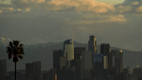 A helicopter flies above the Los Angeles downtown skyline as snow-topped mountains stand after sunrise following heavy rains as seen from the Kenneth Hahn State Recreation Area on December 29, 2020 in Los Angeles, California. (Photo by Patrick T. FALLON / AFP) (Photo by PATRICK T. FALLON/AFP via Getty Images)