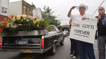 Un admirador del legendario jefe del crimen John Gotti saluda y sostiene un cartel que dice "John Gotti Forever" mientras la procesión fúnebre de Gotti pasa por el Bergin Hunt and Fish Club el 15 de junio de 2002 en Queens, Nueva York.