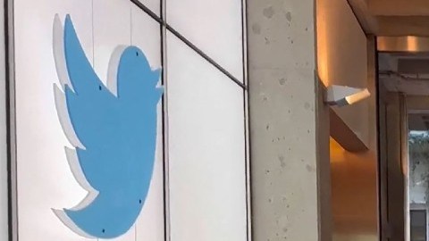 Una foto de Elon Musk en medio de un pasillo con escritorios y un logotipo de Twitter.