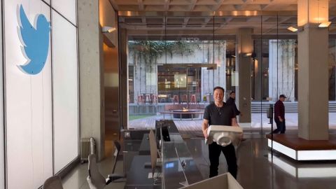 Una foto de Elon Musk en medio de un pasillo con escritorios y un logotipo de Twitter.