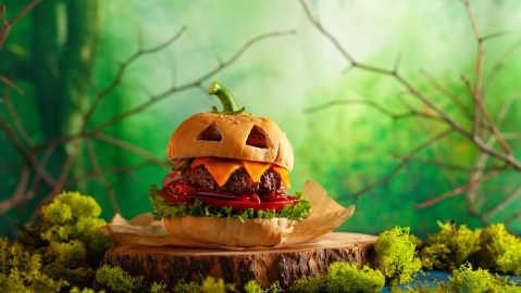 Imagen de una hamburguesa en forma de calabaza en medio de un bosque con neblina.