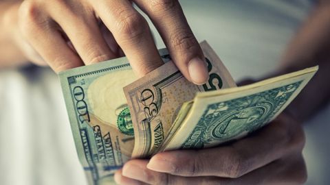 Imagen de unas manos que cuentan billetes de dólar.