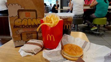 Imagen de un paquete de comida de McDonalds con una bolsa de papel, unas papas, un vaso con refresco y una hamburguesa.