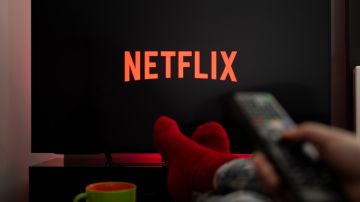 Imagen de una persona que mantiene sus pies sobre una mesa frente a una pantalla en la que se ve un logotipo de la plataforma Netflix.