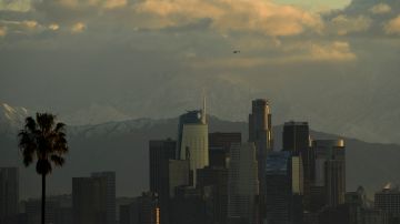 A helicopter flies above the Los Angeles downtown skyline as snow-topped mountains stand after sunrise following heavy rains as seen from the Kenneth Hahn State Recreation Area on December 29, 2020 in Los Angeles, California. (Photo by Patrick T. FALLON / AFP) (Photo by PATRICK T. FALLON/AFP via Getty Images)