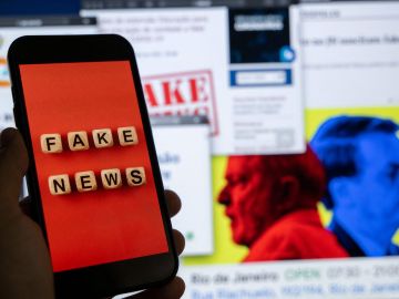 La imagen ilustrativa muestra la pantalla de un teléfono inteligente con la frase "Noticias falsas" en inglés.