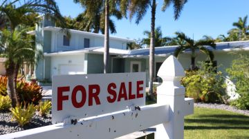 Imagen de un letrero de venta frente a una vivienda de color blanco.