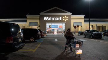 Imagen de una persona que camina empujando un carro de supermercado en medio de un estacionamiento en una tienda Walmart.