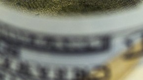 Imagen de varios billetes extendidos y enrollados, sobre una hoja de medición de indicadores financieros.