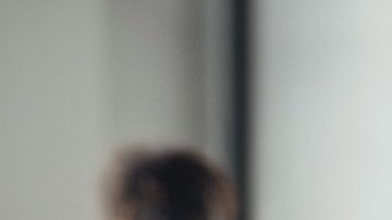 Imagen de una persona que carga una caja de cartón y en el fondo otra, fuera de foco, empaca para una mudanza.