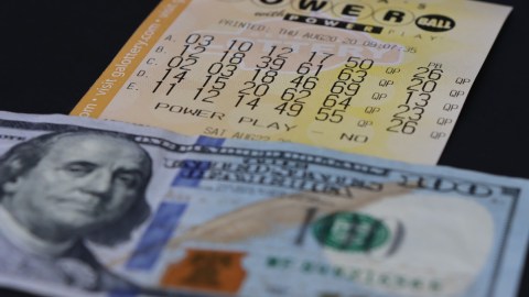 Imagen de un boleto de la lotería Powerball debajo de un billete de $100 dólares.