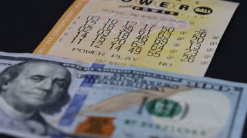 Imagen de un boleto de la lotería Powerball debajo de un billete de $100 dólares.