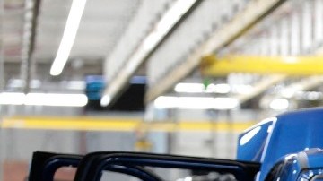 Imagen de una línea de producción de vehículos en donde una persona manipula un auto en fabricación.