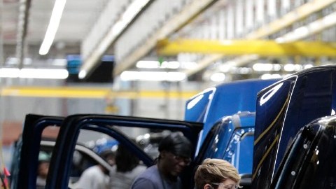Imagen de una línea de producción de vehículos en donde una persona manipula un auto en fabricación.