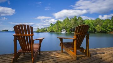 Imagen de dos sillas sobre un muelle frente a un lago.