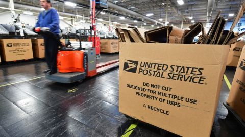 Imagen de una oficina de gestión de paquetes del Servicio Postal de los Estados Unidos, en la que se ve una caja en primer plano y trabajadores en segundo.