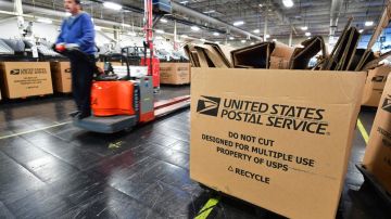 Imagen de una oficina de gestión de paquetes del Servicio Postal de los Estados Unidos, en la que se ve una caja en primer plano y trabajadores en segundo.