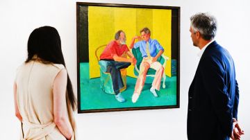 Imagen de dos personas que miran a la distancia un cuadro en el que hay otras dos personas sentadas en sillones de color verde.