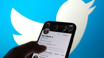 Una mano sostiene un teléfono en el que se ve el perfil de Elon Musk de la red social Twitter y en el fondo el logotipo de la compañía.