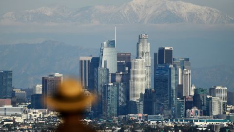 TOPSHOT - A person looks toward snow-topped mountains behind the Los Angeles downtown skyline following heavy rains, as seen from the Kenneth Hahn State Recreation Area on December 15, 2021 in Los Angeles, California. (Photo by Patrick T. FALLON / AFP) (Photo by PATRICK T. FALLON/AFP via Getty Images)