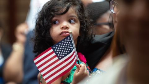 Una niña pequeña sostiene la bandera mientras USCIS da la bienvenida a nuevos ciudadanos.