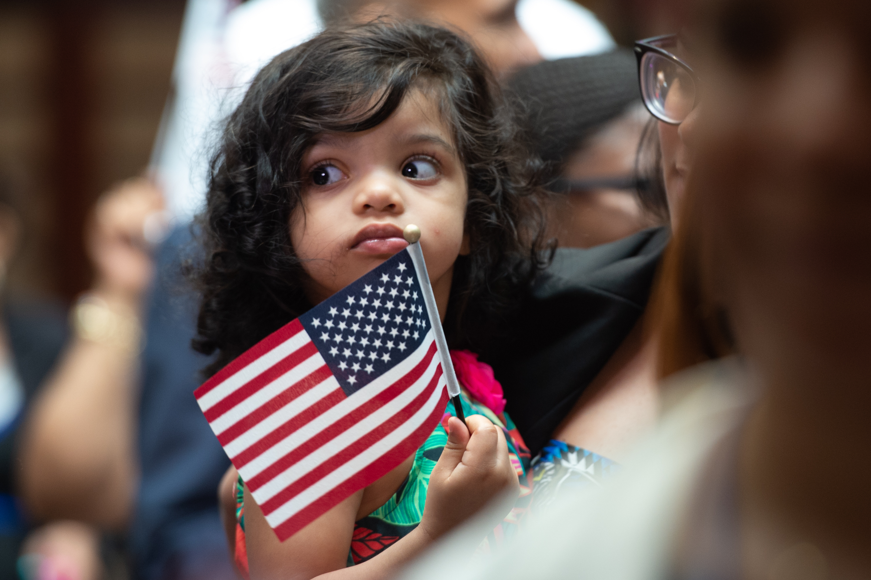 A little girl holds a flag as USCIS welcomes new citizens.