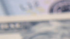 Imagen de un celular que está sobre unos billetes de color verde y en su pantalla de ve el logotipo de la empresa Airbnb en blanco con rojo.